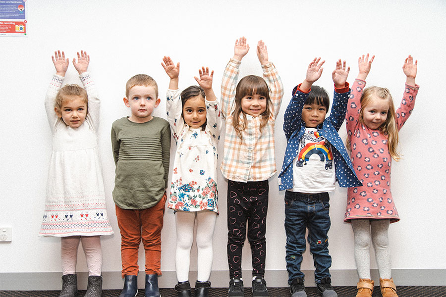 Happy kids, 6 preschoolers standing in a line with their hands in the air