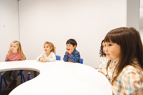 Develop A Love Of Learning, featuring 5 kids in a Shichida class, sitting at a table, observing their teacher demonstrating something off view