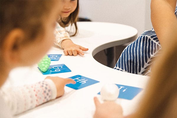 Early Literacy Skills for kids, featuring young children playing a phonics game, matching objects to letter cards in a Shichida class