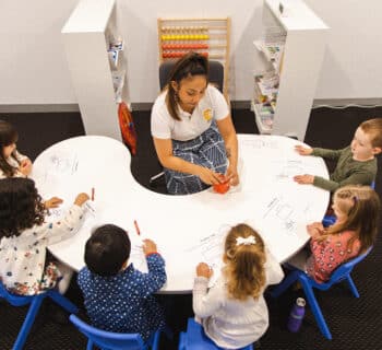 Pre-Primary Classes Australia, featuring a classroom with 6 kids and a teacher sitting around a table