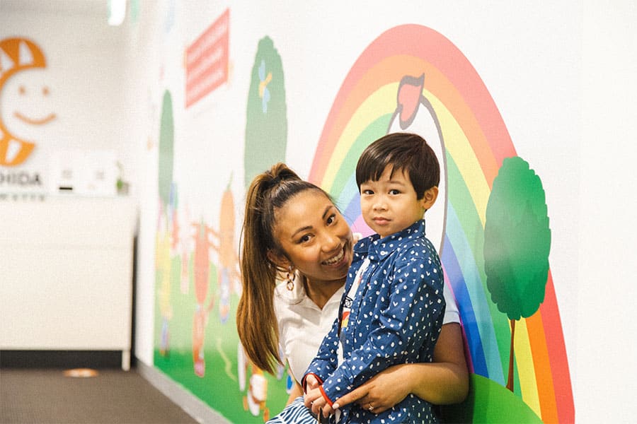 Friendly Shichida teacher and young student posing in front of a rainbow mural