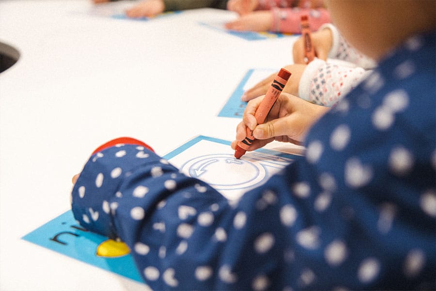 Young kids tracing numbers on laminated sheets using red crayons