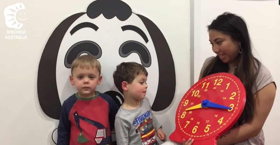 A teacher showing 2 young boys a large analogue clock used to teach reading of time