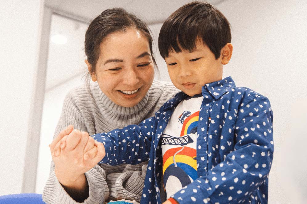 A mum holding her young son's hand in a Shichida class, while they bond and have fun together