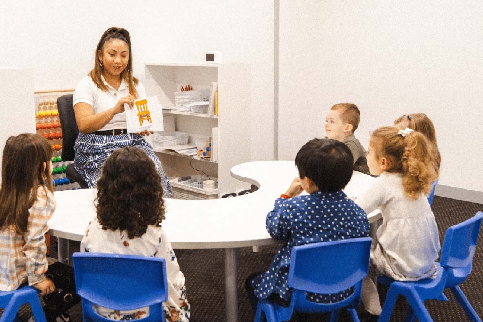 Six kids in a Shichida class watching a teacher that is holding flashcards