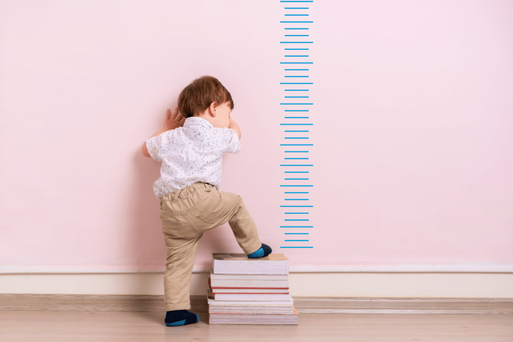 Understanding Child Development, showing a little toddler boy climbing a stack of books while leaning against a pink wall