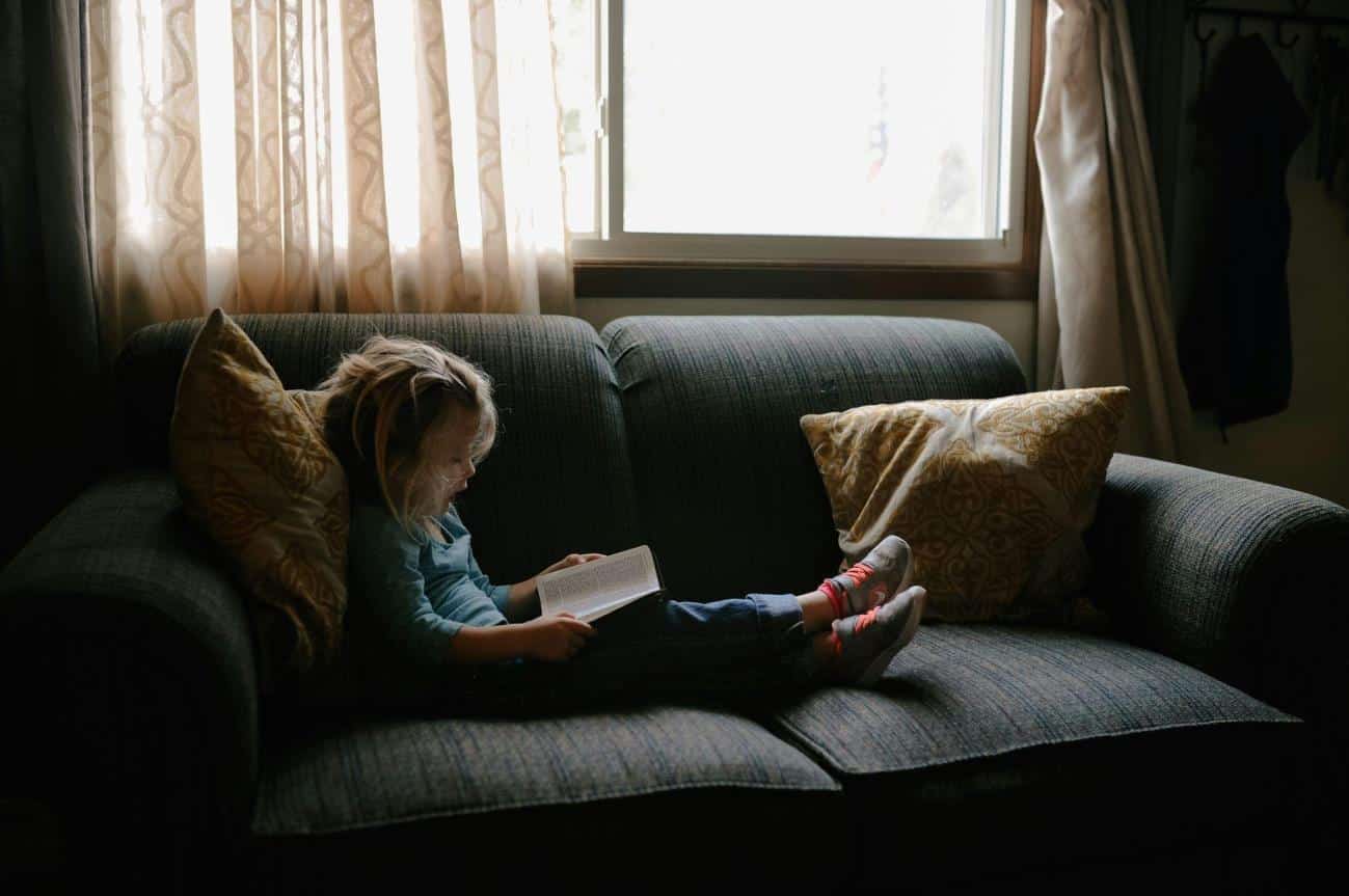 girl reading book sitting on sofa - sight words flash cards teaches reading