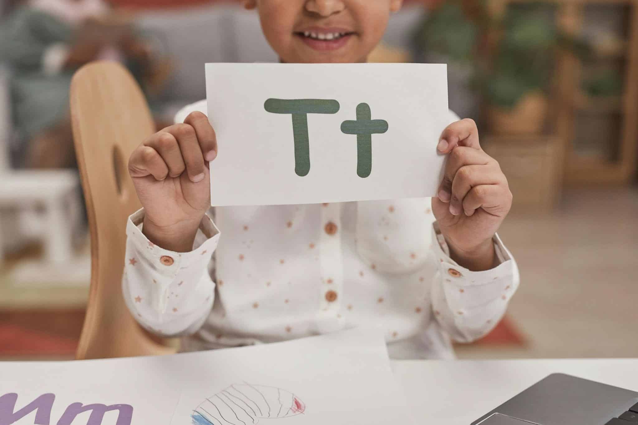 The letter T on alphabet flashcards, held up by a preschooler