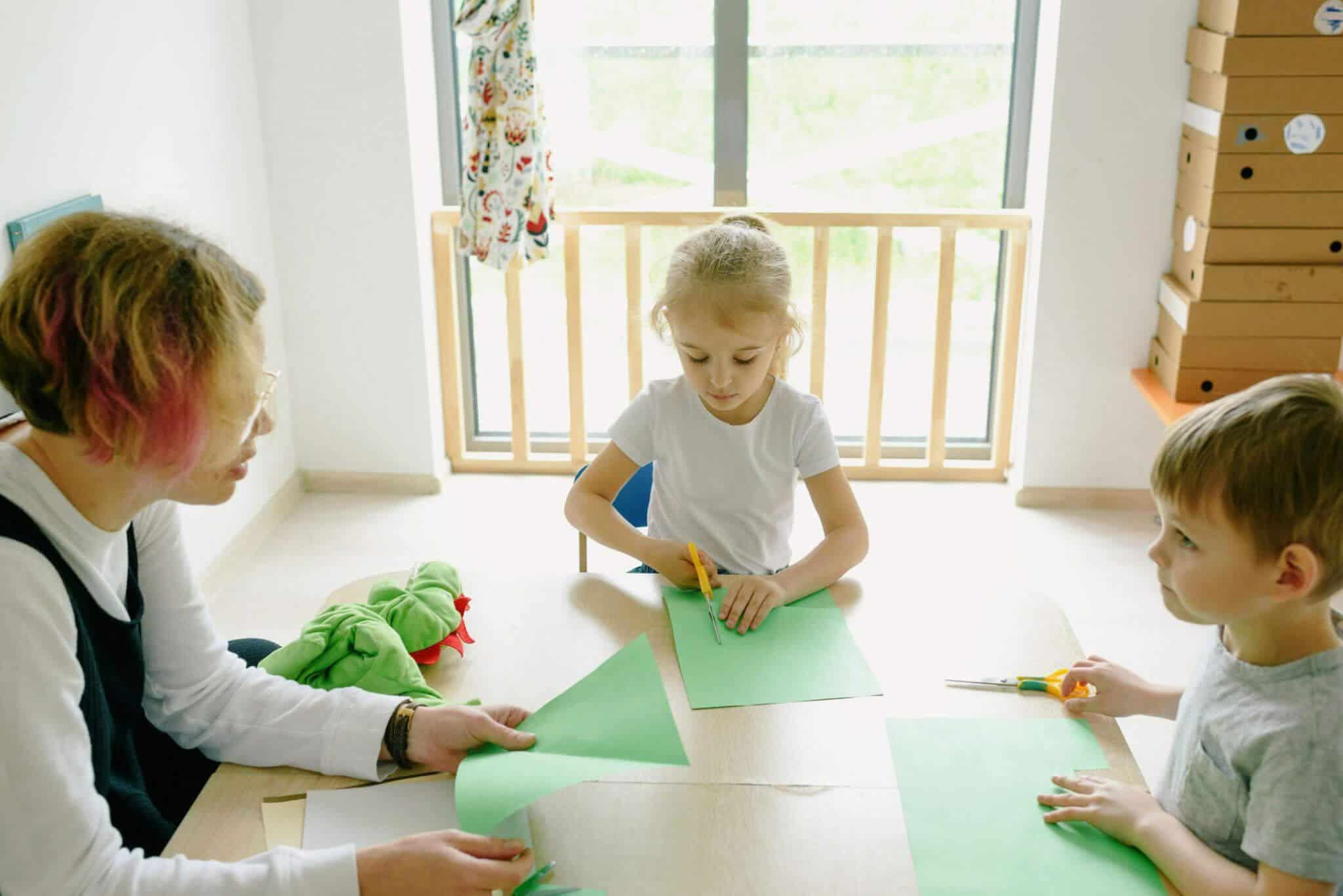 An adult and two preschoolers, cutting out paper in a classroom environment.