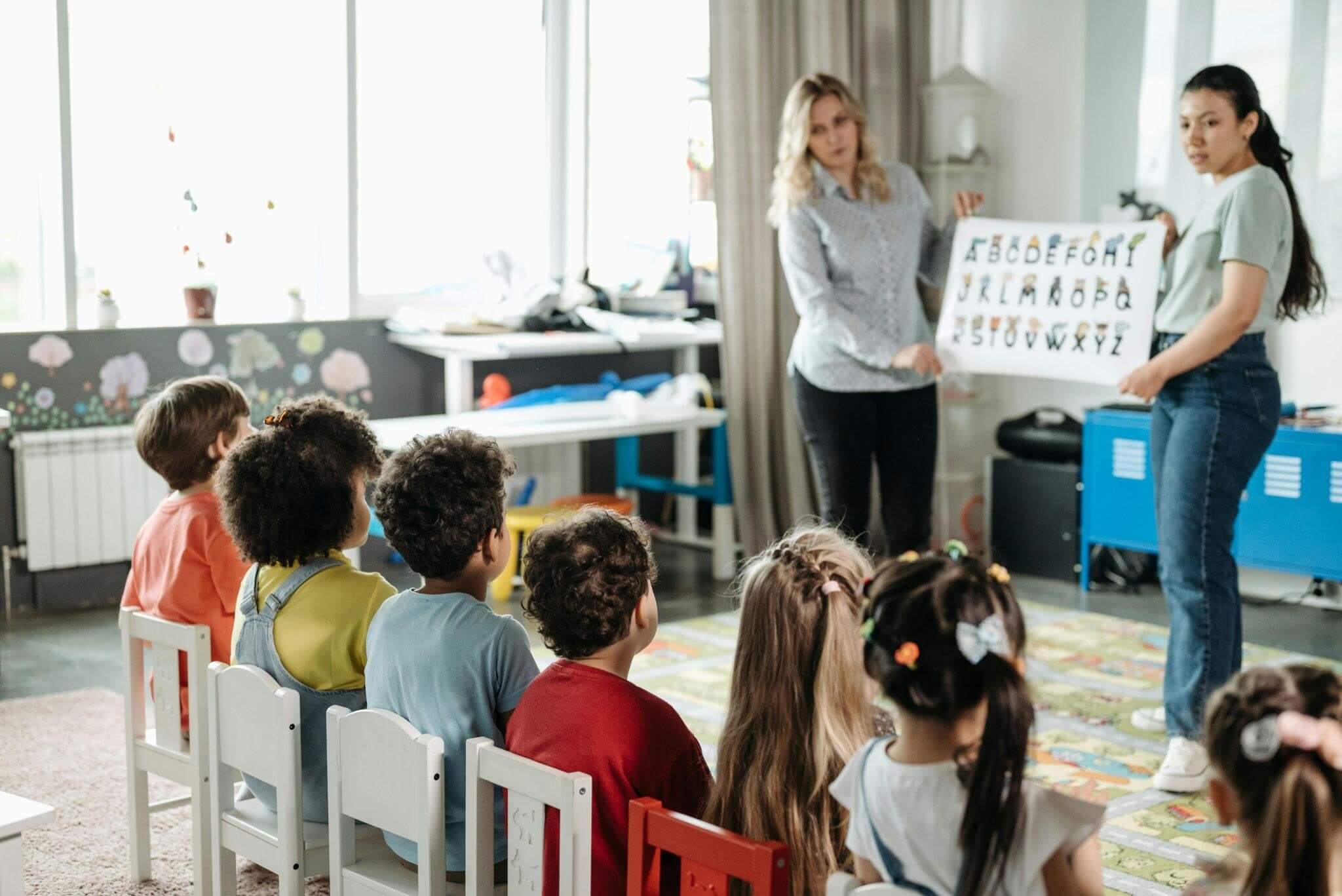Keep alphabet activities for preschoolers creative and fun, featuring 2 adults holding up an alphabet poster for preschoolers.