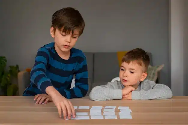 Two young boys sitting at a wooden table and playing with flashcards.