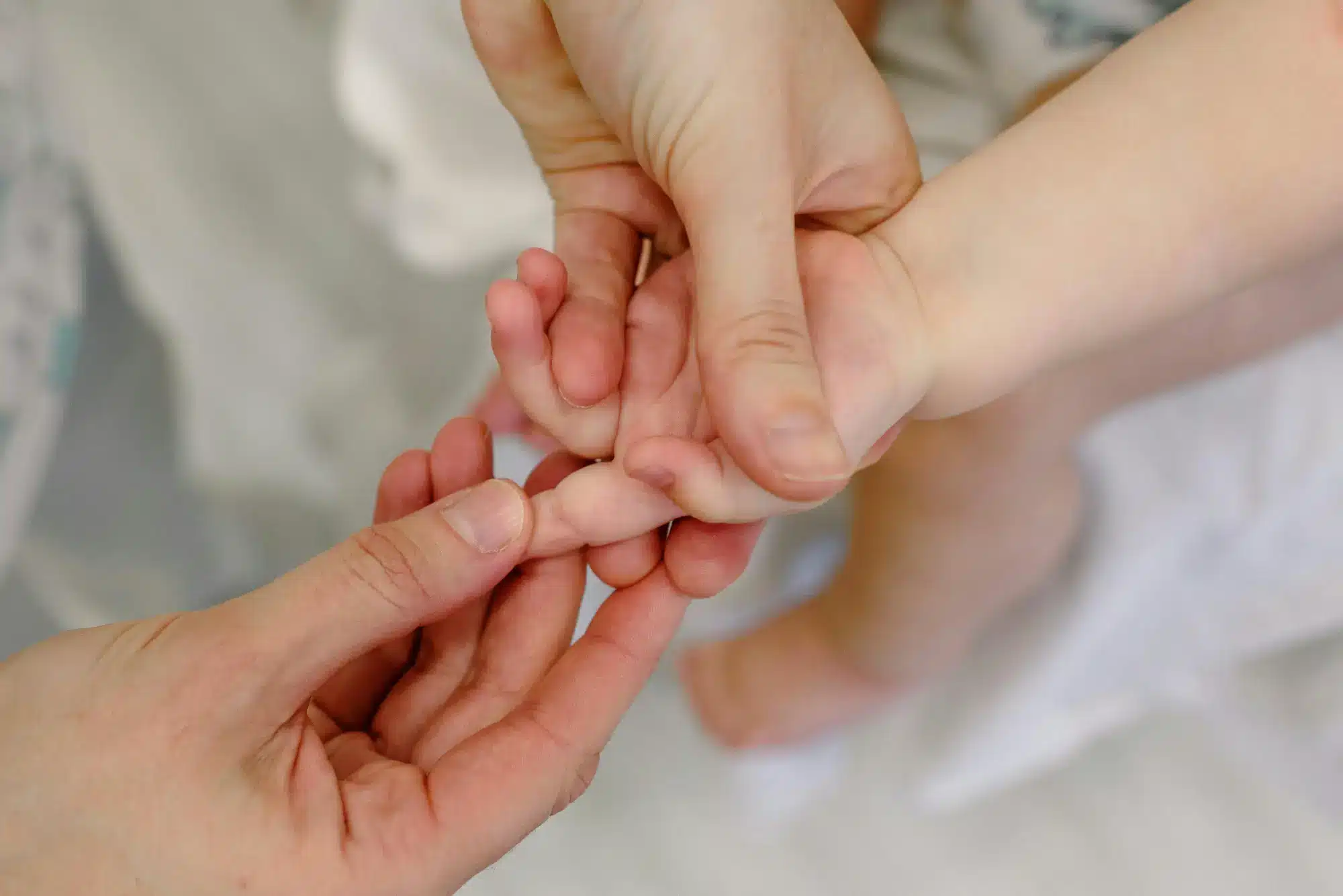 A close-up of an adult's hands gently holding the small hand of a child.