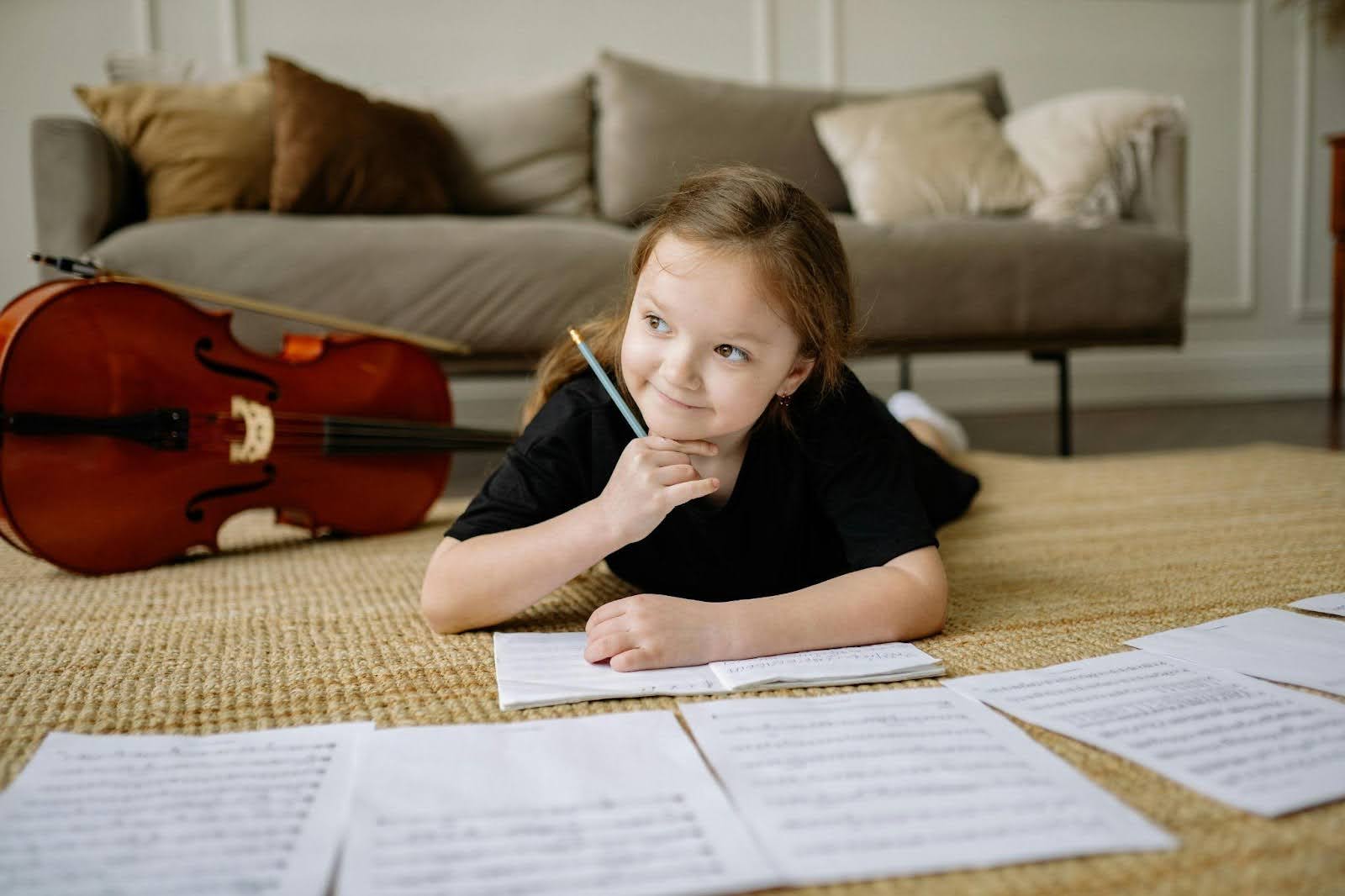 Average IQ for kids - A young girl lying on a rug, thoughtfully holding a pencil with music sheets spread around her and a cello resting on the floor nearby.