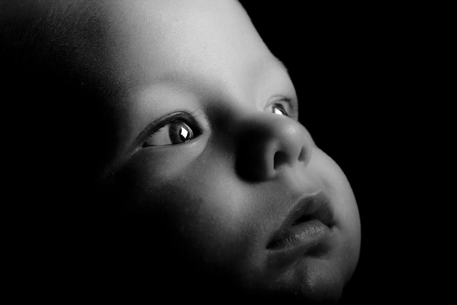Baby eye development timeline, Close-up black and white photograph of a baby gazing upward, with dramatic lighting illuminating the face against a dark background.