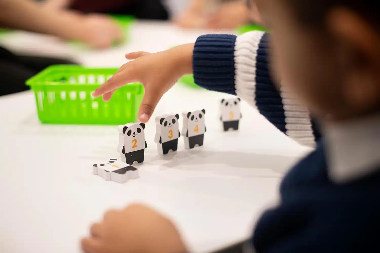 A child's hand reaches to move small wooden panda figurines, each marked with a number (1, 2, 3, 4), during a learning activity on a white table.