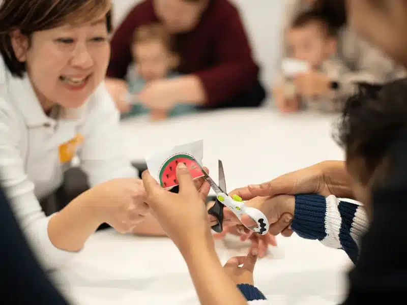Fine motor development - Image by Shichida: A preschooler practising cutting along a rounded edge using safety scissors during a Shichida class.